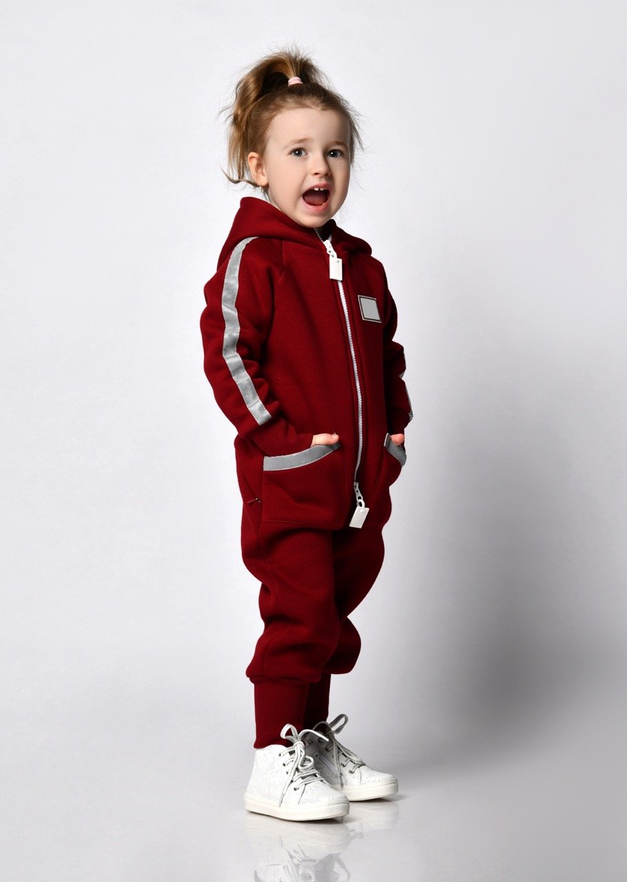 Cute adorable little preschool girl with European appearance in trendy sportswear holding her hand in her pocket, full length portrait on space studio background. Children's fashion