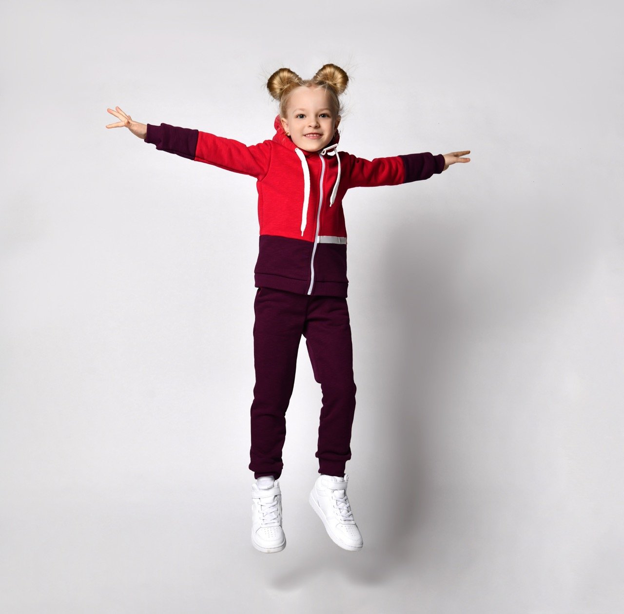Cheerful photograph of a little girl jumping high in warm fleece sportswear and sneakers isolated on a white background. Advertising of children's fashionable clothes. Great design for fashion store
